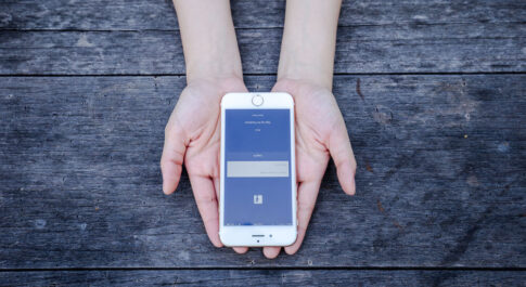 iPhone z włączonym Facebookiem na dłoniach
