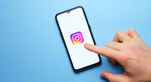 telefon z logo Instagrama, które ktoś wskazuje palcem, na niebieskim tle