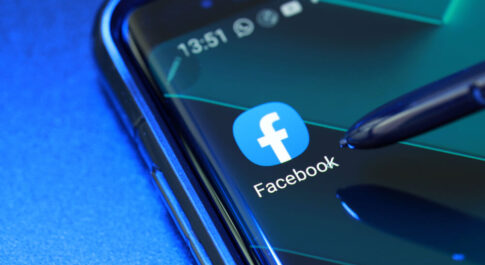 logo aplikacji Facebook na pulpicie telefonu. Telefon leży na niebieskim tle