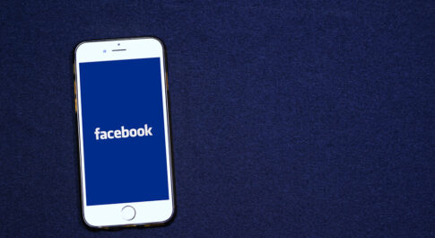 biały iPhone z granatowym tłem wraz z logo Facebooka, na granatowym tle.