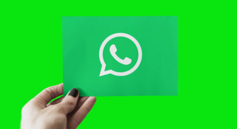 Zielona karteczka z białym logo Whatsappa na zielonym tle. Trzyma ją ręka z pomalowanymi na czarno paznokciami.