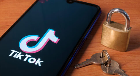 Smartfon z logo TikToka na wyświetlaczu, leżący na drewnianym blacie. Obok stoi kłódka i leżą klucze.