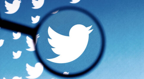 Na niebieskim tle dużo Białych ptaków, symboli Twittera. Jeden z nich pokazany jest pod lupą.