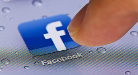 Palec dotykający ikonę Facebooka.