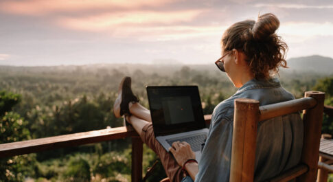 Kobieta siedząca przed komputerem na balkonie z widokiem na horyzont.