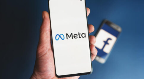 Na pierwszym planie ręka trzymająca telefon z włączony logo Mety. Na drugim, kolejny telefon z włączonym logo Facebooka.