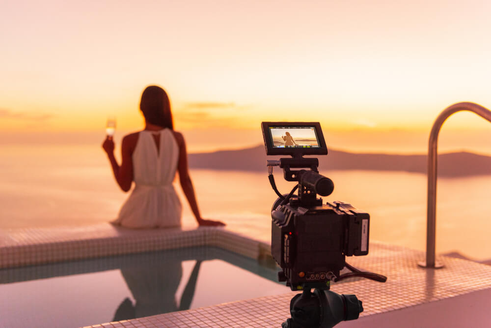 Kobieta siedząca tyłem, patrząca na morze. Za nią ustawiony aparat, którym zrobi sobie zdjęcie.