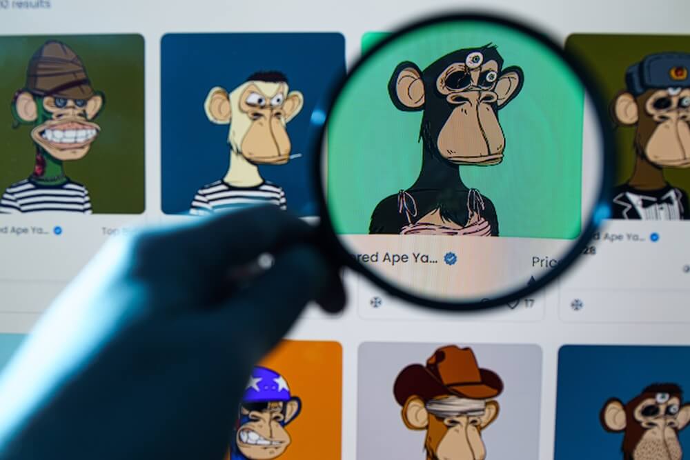Na monitorze kilka obrazów NFT. Jeden, z małpą, jest pod lupą, którą trzyma ręka w kolorach retro.