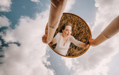 Dziewczyna odbijająca się w lustrze, które trzyma przed sobą, na tle nieba. Najlepsze kampanie w social mediach 2021.