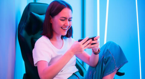 Dziewczyna siedząca na fotelu gamingowym, grająca w gry na telefonie, ze słuchawkami na uszach. - trendy w gamingu