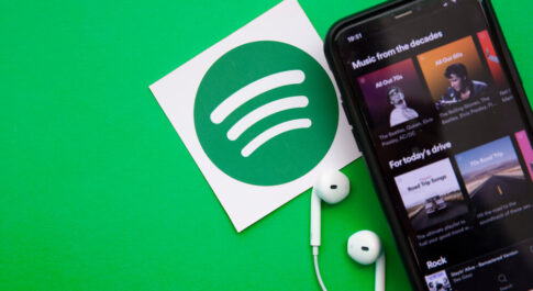 Telefon z włączoną muzyką, na zielonym tle. Obok kartka z logo Spotify.
