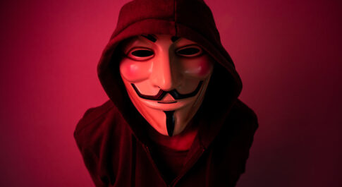 Człowiek w masce Anonymous, w kapturze i czerwonym świetle.