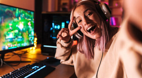 Gamerka robiąca sobie selfie w słuchawkach i obok komputera, gdzie włączona jest gra.