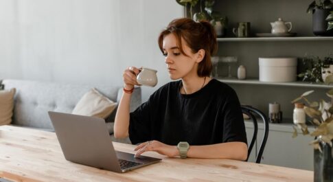 Kobieta na home office, pijąca kawę przy laptopie.
