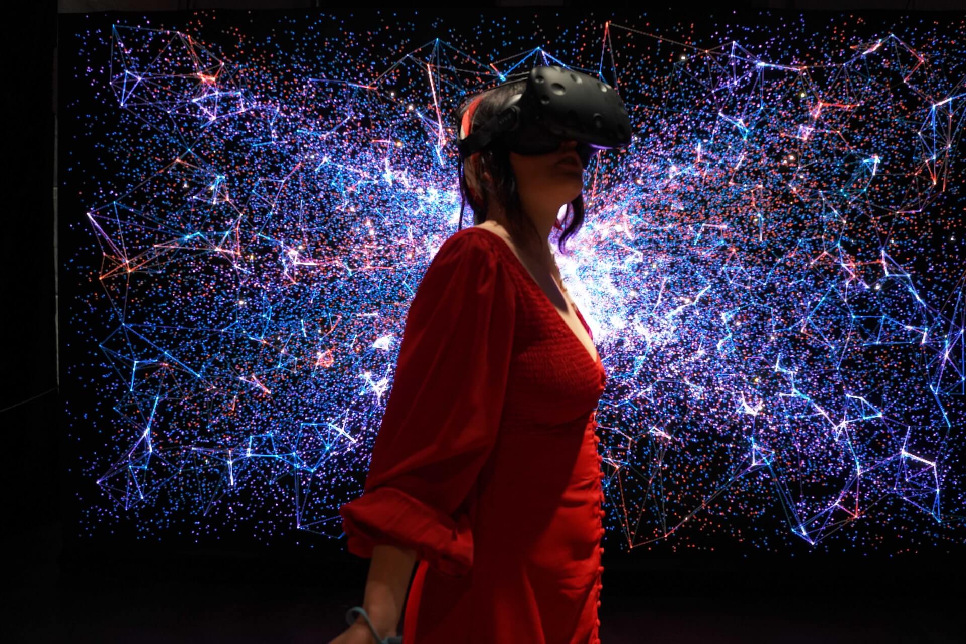 Kobieta z okularami VR, na tle galaktyki. Ubrana w czerwoną sukienkę. 