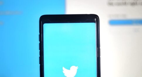 Telefon z włączonym Twitterem, widocznym logo. W tle komputer z włączonym Twitterem, widać post.