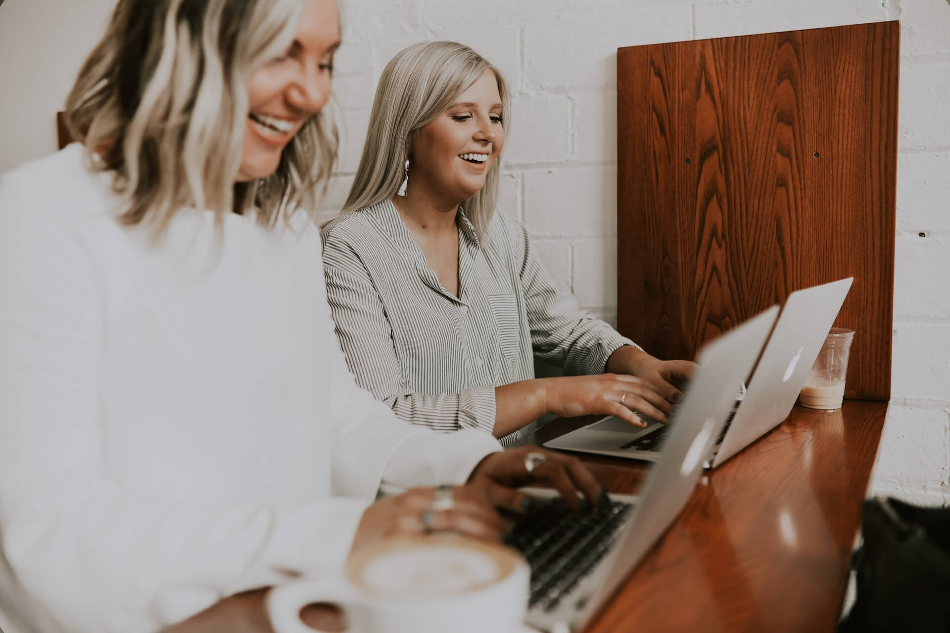 Dwie kobiety siedzą uśmiechnięte przed laptopami. 
