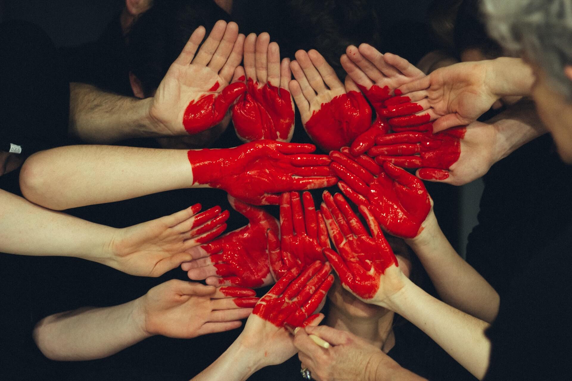 Wiele dłoni należących do różnych ludzi. Na nich namalowane jest czerwone serce. 