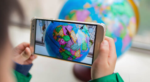 Chłopiec mający telefon z dłoni. Korzysta z efektu AR. Telefon jest skierowany w stronę globusa.