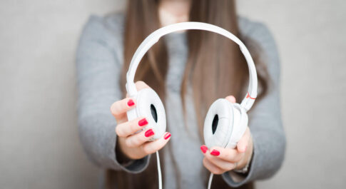 Dziewczyna trzymająca w rękach białe słuchawki na uszy.