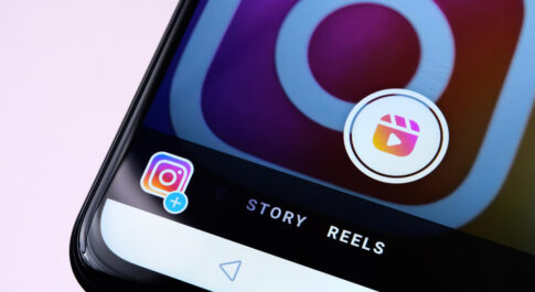 Telefon leżący na różowym tle. Widać ikonę Instagram oraz zakładki Story i Reels.