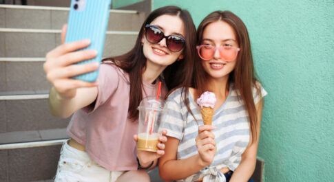 Dwie młode dziewczyny robiące sobie selfie. Jedna trzyma loda, druga mrożoną kawę.