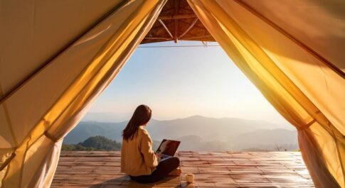 Kobieta z laptopem, siedząca w namiocie i patrząca na horyzont.