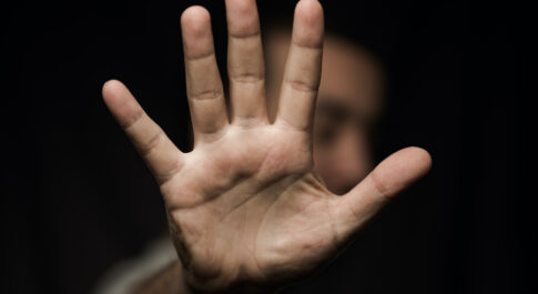 Dłoń mężczyzny na czarnym tle symbolizująca STOP